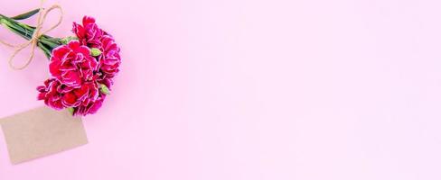 maggio festa della mamma idea concept photography - bellissimi garofani in fiore legati da fiocco con carta di testo kraft isolata su un tavolo moderno e luminoso, spazio per la copia, distesi, vista dall'alto, mock up foto