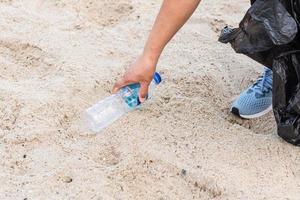 donna pulisce raccogliendo bottiglie di plastica in spiaggia. concetto di protezione dell'ambiente, salvataggio del mondo, riciclaggio, riduzione del riscaldamento globale. primo piano, sfondo sfocato, copia spazio a sinistra foto