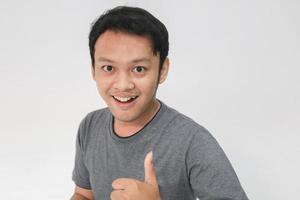 il giovane uomo asiatico indossa una camicia grigia con la faccia sorridente felice e i pollici in su foto