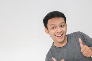 il giovane uomo asiatico indossa una camicia grigia con la faccia sorridente felice e i pollici in su foto