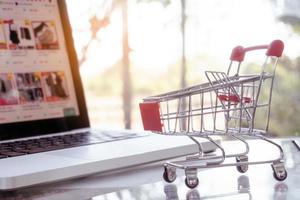 concetto di shopping online - carrello o carrello e laptop sul tavolo foto