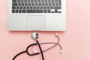 computer portatile tastiera stetoscopio isolato su sfondo rosa. la moderna tecnologia dell'informazione medica e il concetto di avanzamento del software. diagnostica e riparazione computer e gadget foto