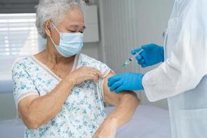 anziana donna anziana asiatica che indossa una maschera facciale che riceve il vaccino covid 19 o coronavirus dal medico fa l'iniezione. foto