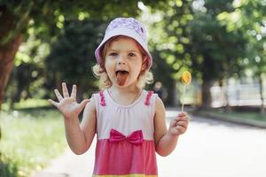 bambino divertente con lecca-lecca caramelle, bambina felice che mangia grande foto