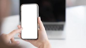 vista ritagliata delle mani della donna che tengono lo smartphone con lo schermo vuoto dello spazio di copia per il messaggio di testo o il contenuto informativo, il messaggio di testo della lettura femminile sul telefono cellulare durante l'ufficio. foto