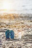 infradito sulla spiaggia di sabbia con acqua in bottiglia di plastica e raggio di sole foto