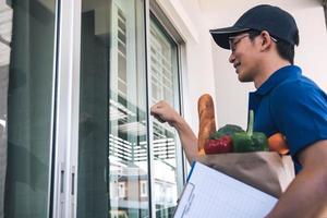 uomo asiatico che tiene un sacchetto di cibo in piedi a bussare alla porta d'ingresso. foto