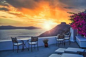 bella vista della caldera e godersi uno scenario romantico tramonto sul mar egeo, santorini. vacanza di viaggio di coppia, destinazione per la luna di miele. romanticismo con fiori, due sedie tavolo e vista mare. vacanza di lusso foto