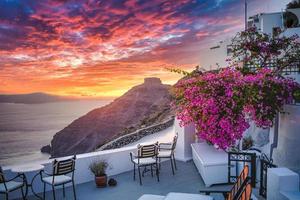 bella vista della caldera e godersi uno scenario romantico tramonto sul mar egeo, santorini. vacanza di viaggio di coppia, destinazione per la luna di miele. romanticismo con fiori, due sedie tavolo e vista mare. vacanza di lusso foto