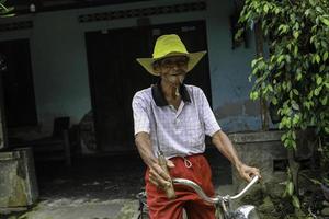 un ritratto di un vecchio contadino indonesiano indossa un cappello giallo con una vecchia bicicletta foto