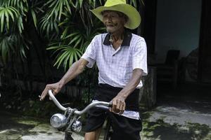 un ritratto di un vecchio contadino indonesiano indossa un cappello giallo con una vecchia bicicletta foto