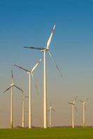 gruppo di grandi turbine eoliche per generare energia elettrica, energia ecologica verde al cielo blu con colori caldi del tramonto in europa. concetto di produzione di energia sostenibile verde. foto
