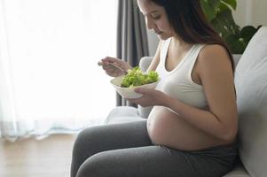 giovane donna incinta che mangia insalata a casa, assistenza sanitaria e gravidanza foto