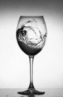 una spruzzata d'acqua in un bicchiere di vino di vetro. spruzzi d'acqua in vetro su sfondo incandescente. schizzi di liquido trasparente nel bicchiere di vino. cibo, oggetto. foto