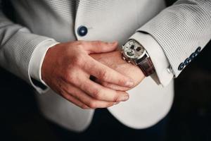 uomo d'affari che controlla il tempo sul suo orologio da polso, uomo che mette l'orologio a portata di mano, lo sposo si prepara al mattino prima della cerimonia di matrimonio. l'uomo mette un orologio. messa a fuoco selettiva foto