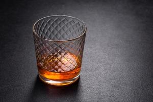 un bicchiere di whisky o cognac su un tavolo di cemento nero. momento relax foto