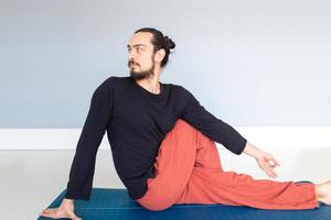 giovane uomo bianco dai capelli lunghi caucasico sta eseguendo yoga in uno studio o in una casa. foto