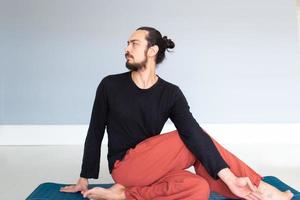 giovane uomo bianco dai capelli lunghi caucasico sta eseguendo yoga in uno studio o in una casa. foto