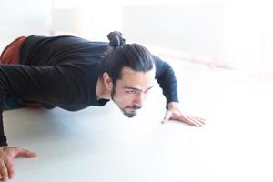 giovane uomo bianco dai capelli lunghi caucasico sta eseguendo yoga in uno studio o in una casa. foto