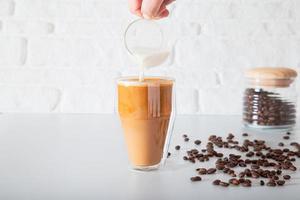 una mano anonima sta versando il latte in un bicchiere di caffè a doppia faccia. foto