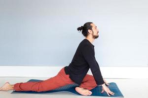 giovane uomo bianco dai capelli lunghi caucasico sta eseguendo yoga in uno studio o in una casa. foto