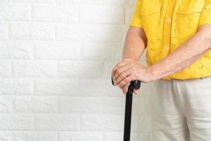 donna anziana asiatica che tiene un bastone da passeggio su sfondo isolato. il concetto di società che invecchia che ha bisogno di tempo e nipoti per tornare a prendersi cura dell'assistenza sanitaria foto