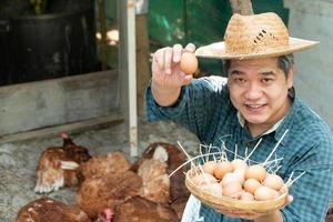 gli agricoltori asiatici tengono un cesto di uova con la mano sinistra e la mano destra che tiene l'uovo e tiene in alto. in un allevamento di polli nella propria zona di origine foto