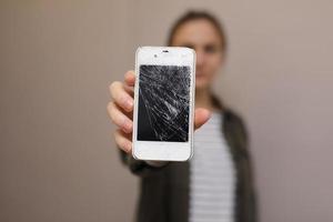 frustrato giovane donna tenendo il cellulare con il vetro dello schermo rotto. il display del telefono deve essere riparato. isolato su sfondo grigio. messa a fuoco selettiva su smartphone foto