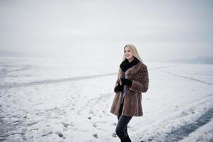 ritratto di giovane eleganza ragazza bionda in uno sfondo di pelliccia fiume nebbioso sul ghiaccio d'inverno. foto