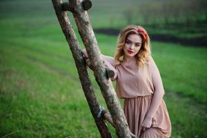 yong eleganza ragazza bionda al vestito rosa sullo sfondo del giardino scala in legno. foto