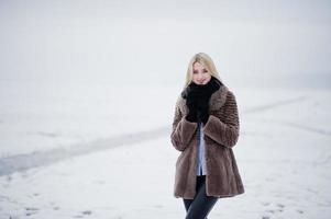 ritratto di giovane eleganza ragazza bionda in uno sfondo di pelliccia fiume nebbioso sul ghiaccio d'inverno. foto