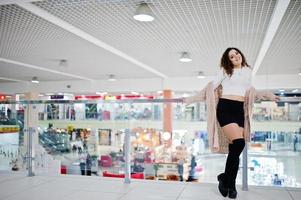 giovane modella riccia posata su minigonna in un grande centro commerciale vicino a ringhiere di vetro. foto