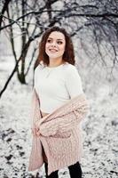 sfondo ragazza bruna riccia neve che cade, indossare un maglione caldo lavorato a maglia, minigonna nera e calze di lana. modello in inverno. ritratto di moda con tempo nevoso. foto dai toni di instagram.