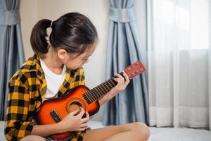 bambina suona la chitarra, bambina che impara a suonare la chitarra in camera da letto, hobby per bambini foto