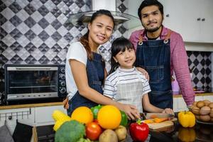 la famiglia felice ha papà, mamma e la loro piccola figlia che cucinano insieme in cucina foto