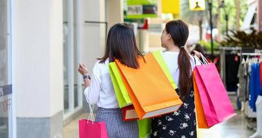 le donne asiatiche con un amico tengono in mano le borse della spesa e usano uno smartphone e sorridono mentre fanno la spesa al supermercato