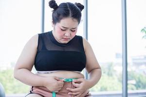 donna asiatica in sovrappeso che misura lo strato di grasso con il giro vita a casa foto
