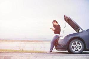 la donna asiatica sta usando un telefono per chiamare il meccanico dell'auto. per riparare le auto danneggiate sulla strada foto