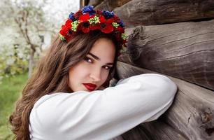 giovane bella donna con lunghi capelli scuri in blusa ucraina e in una corona in un villaggio etnico all'aperto a kyiv ucraina foto