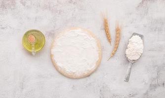 gli ingredienti per l'impasto della pizza fatta in casa con spighe di grano, farina di grano e chicchi di grano installati su sfondo bianco di cemento. la nostra e farina di grano bianco in una ciotola di legno impostata su sfondo bianco di cemento. foto