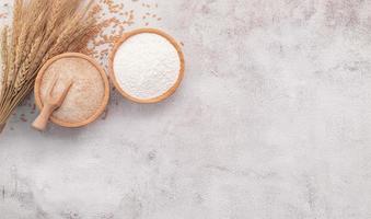 chicchi di grano, farina di grano marrone e farina di grano bianco in una ciotola di legno allestita su sfondo bianco di cemento. foto