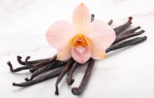 bastoncini di vaniglia essiccati e fiori di orchidea allestiti su fondo di marmo. foto