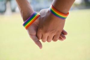 braccialetti di gomma arcobaleno nei polsi di una coppia di ragazzi asiatici con sfondo sfocato, concetto per la celebrazione della comunità lgbt nel mese dell'orgoglio o nel giugno in tutto il mondo. foto