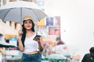 la giovane donna adulta asiatica con l'ombrello usa lo smartphone per viaggiare a Bangkok. foto