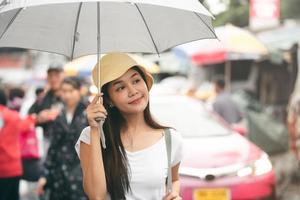 il giovane viaggiatore asiatico adulto tiene l'ombrello quando piove in una strada pedonale. foto