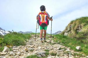 il ragazzino cammina sul sentiero di montagna durante un'escursione. con lo zaino foto