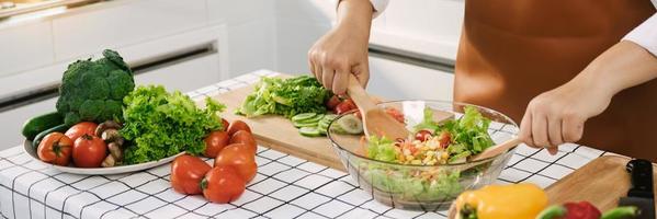 la donna asiatica sta mescolando gli ingredienti in un'insalatiera al tavolo da cucina della cucina. foto