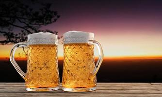 bicchiere da birra chiaro con birra fredda piena e schiuma all'imboccatura del bicchiere e goccioline d'acqua aderiscono ai bordi. tavolato o superficie in legno e con paesaggi montani al sole del mattino. rendering 3D
