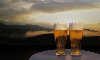 Rendering 3d di birra in vetro e vista sulle montagne sullo sfondo con tramonto e nebbia sulla collina in cima. foto