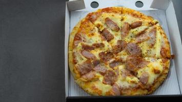 pizza salsiccia e prosciutto formaggio. la pizza nella scatola della livrea giornaliera è stata consegnata sul piano del tavolo in marmo. foto